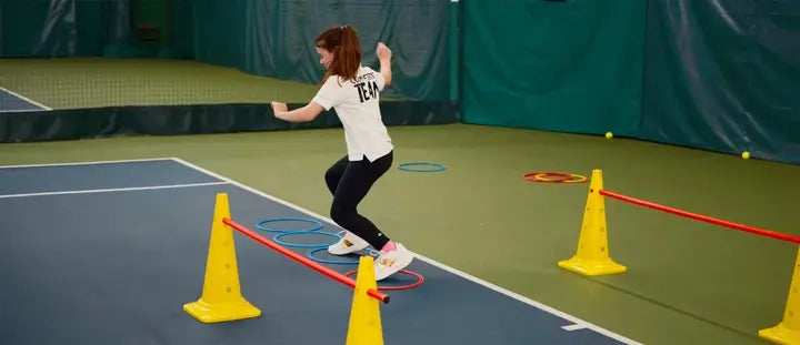 Player practicing agility and footwork drills during tennis lessons at an indoor tennis court