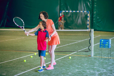 Coach teaching a child tennis fundamentals at an indoor tennis court